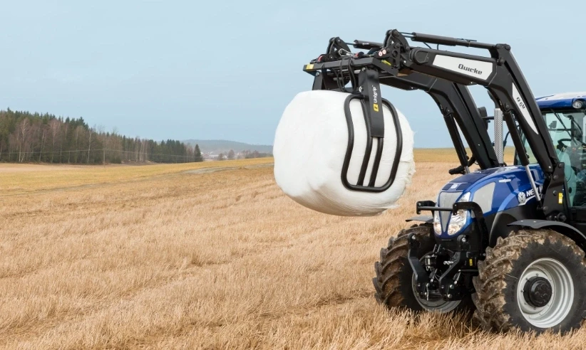Agricultural tractor lifting wrapped hay bale with front loader attachment