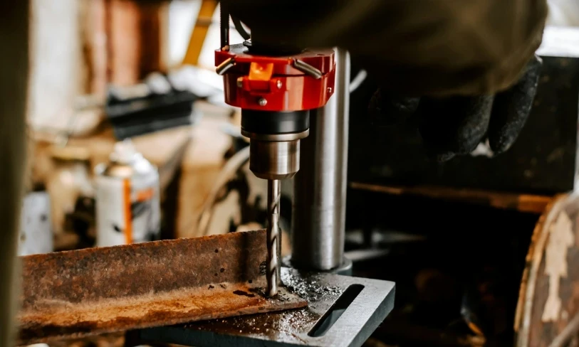 Drill press drilling into a metal beam in a workshop