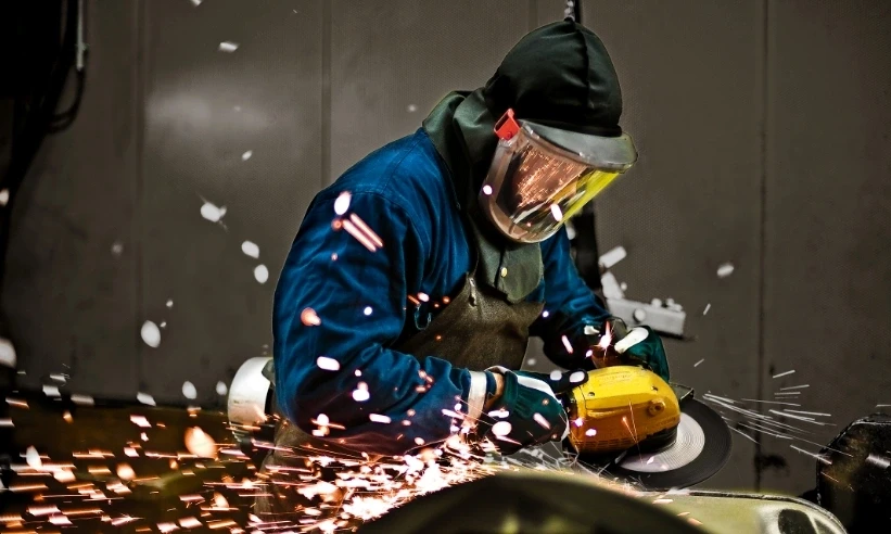 Industrial worker grinding metal component in manufacturing facility
