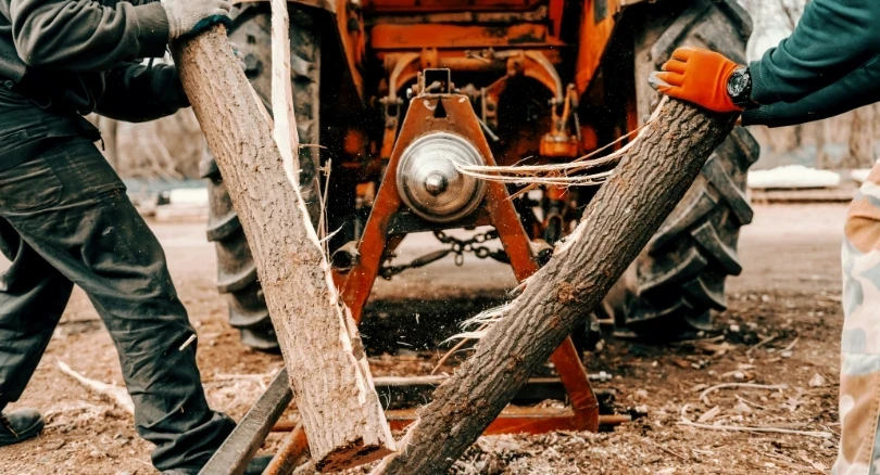 Workers splitting wood logs with tractor-powered log splitter